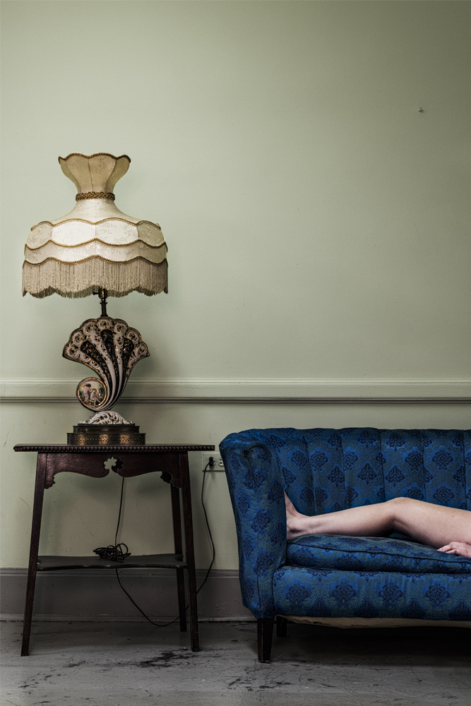 ﻿Legs laying on blue couch next to side table with ornate lamp